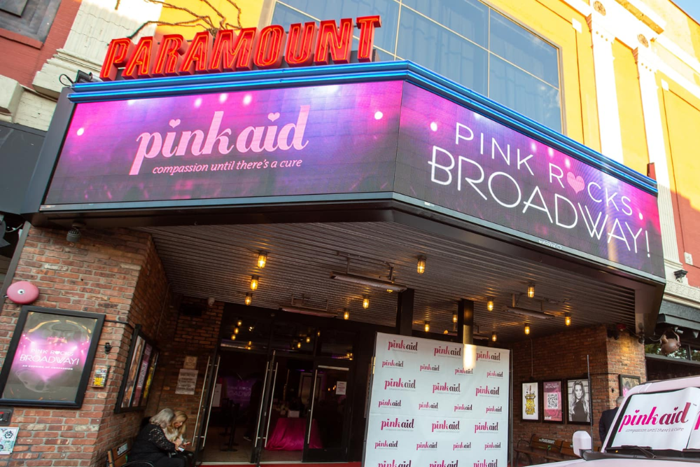 The Paramount Theatre with a pink digital marquee displaying 'pinkaid: compassion until there's a cure' and 'Pink Rocks Broadway!'