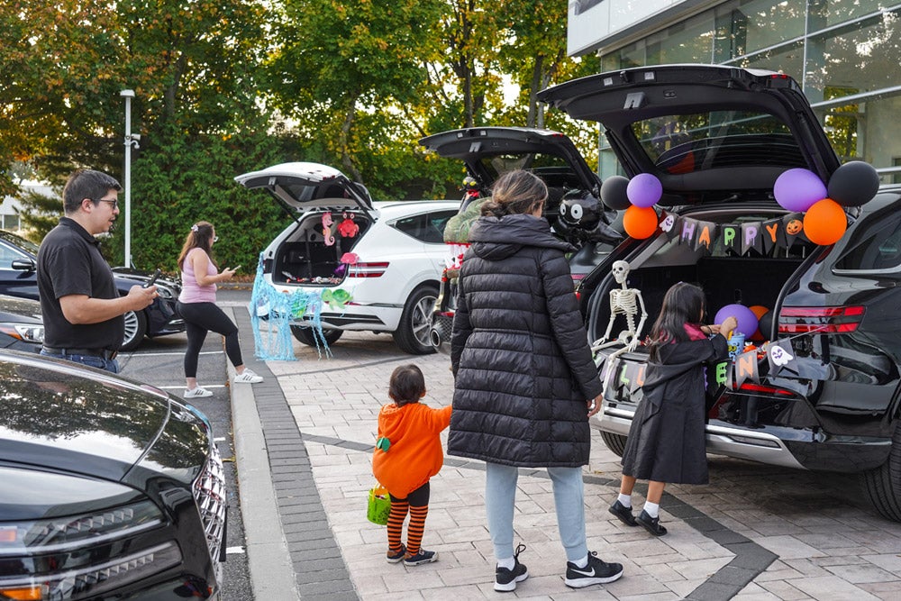 People at a Halloween 'trunk or treat' event with decorated car trunks, including skeletons and balloons.