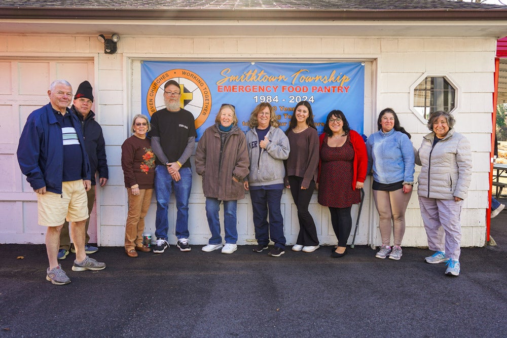 Group of diverse individuals standing in front of a Smithtown Township Emergency Food Pantry banner.