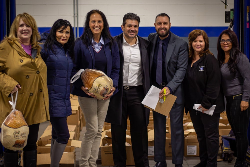Seven people, four women and three men, stand smiling while two women hold turkeys.