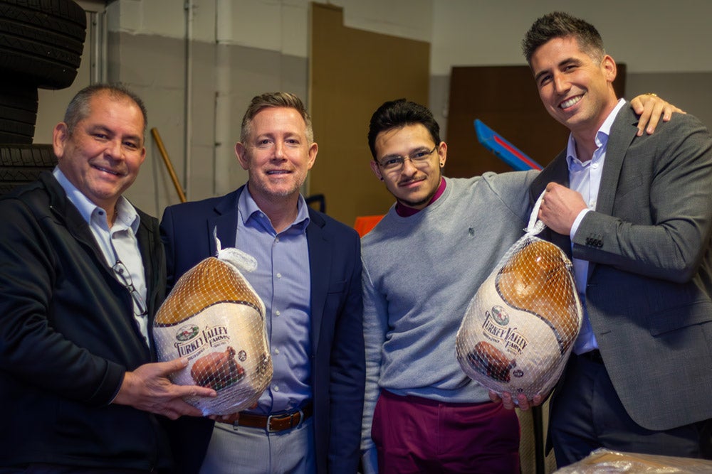 Four smiling men holding unwrapped 'Turkey Valley Farms' turkeys in a warehouse.