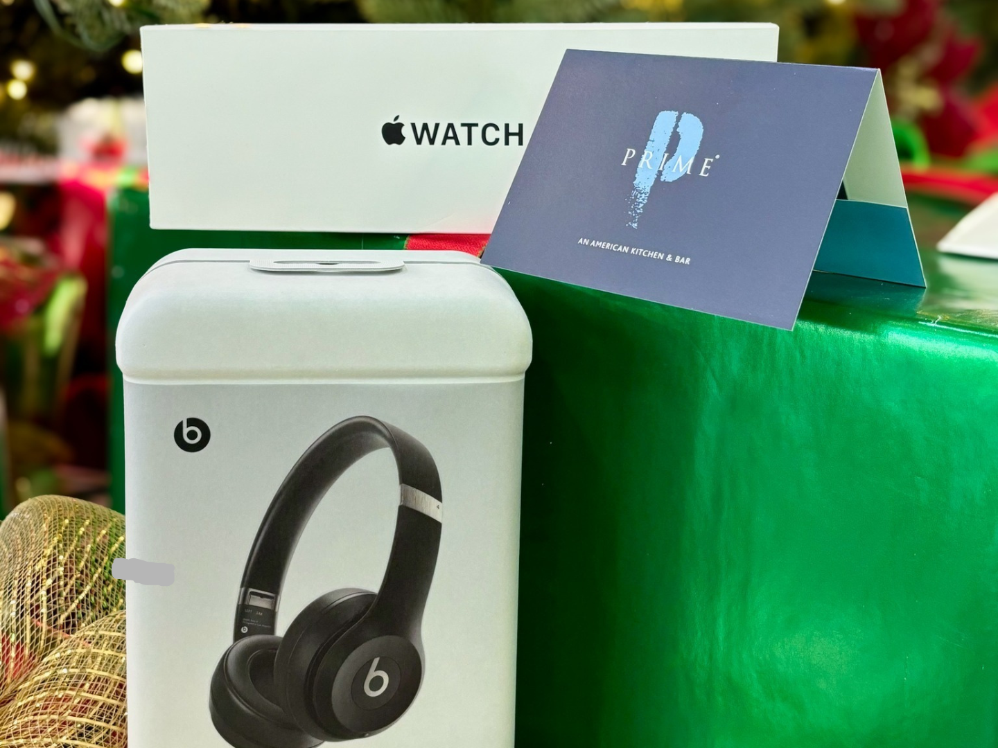 An Apple Watch box, Beats headphones box, and Prime gift card next to a green wrapped present.