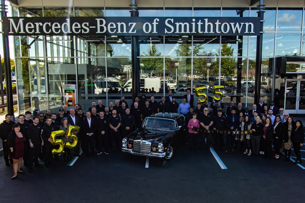 Mercedes-Benz of Smithtown staff posing with a classic Mercedes-Benz and '55' balloons in front of the dealership.
