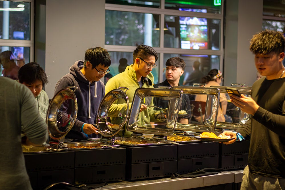 People at a buffet, serving themselves from several chafing dishes on a long table.