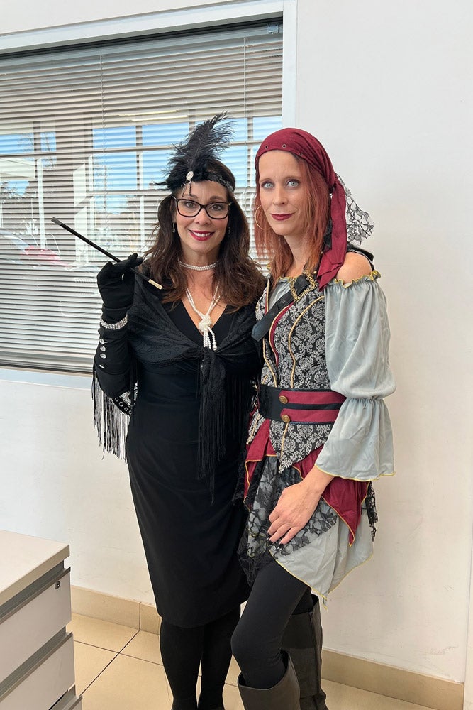 Two women in costumes: one as a flapper in black with a feather headband, one as a pirate with a red bandana.