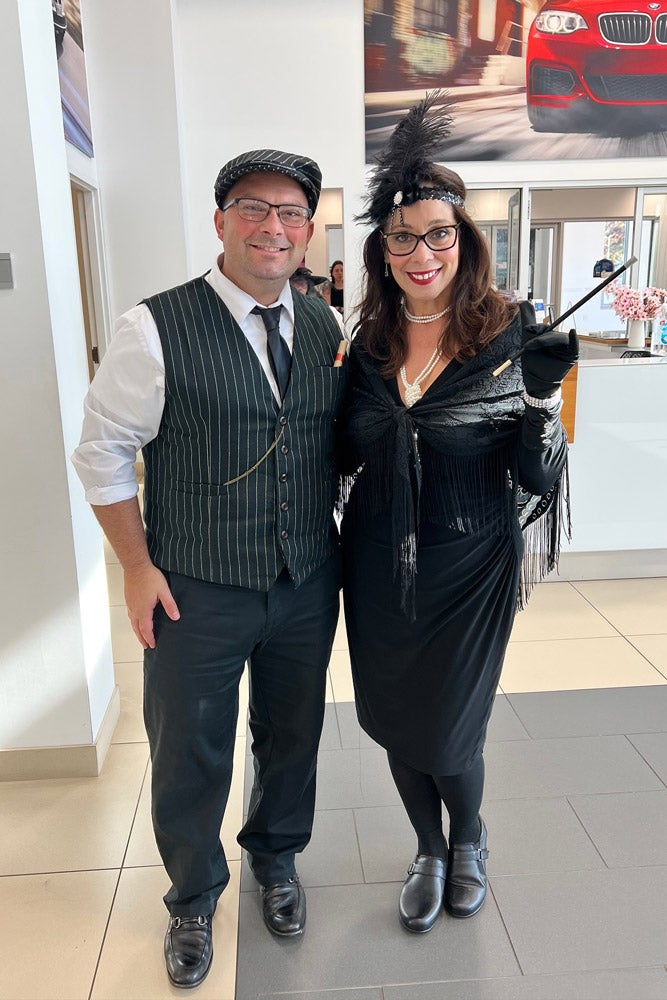 Man in pinstripe vest and flat cap next to woman in flapper dress, feather headband, and long cigarette holder.