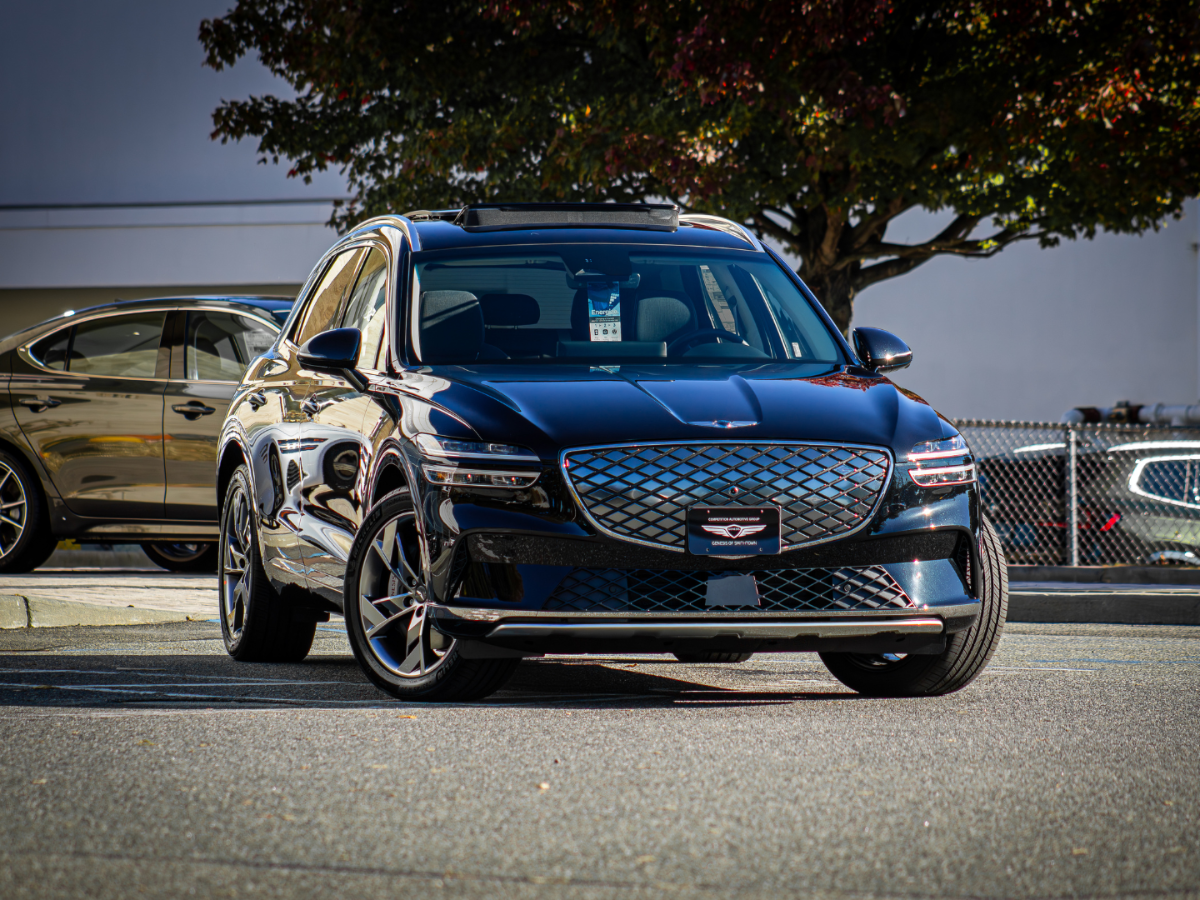A sleek, dark gray SUV with a distinctive diamond-patterned grille parked on asphalt under a tree.