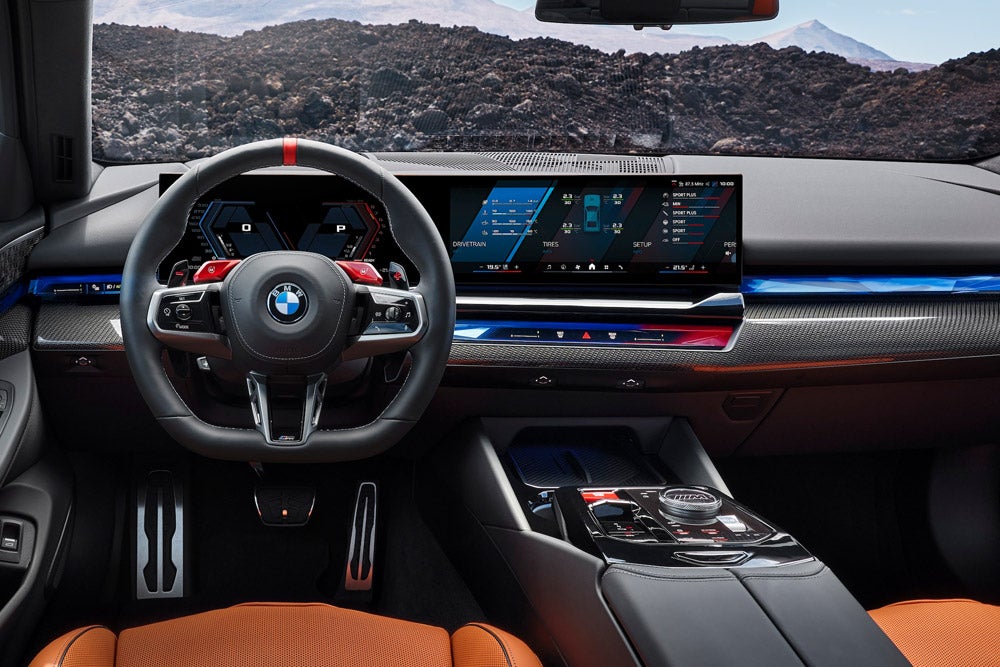 Interior of a modern BMW car with a dark steering wheel, dual digital dashboard, and orange seats.
