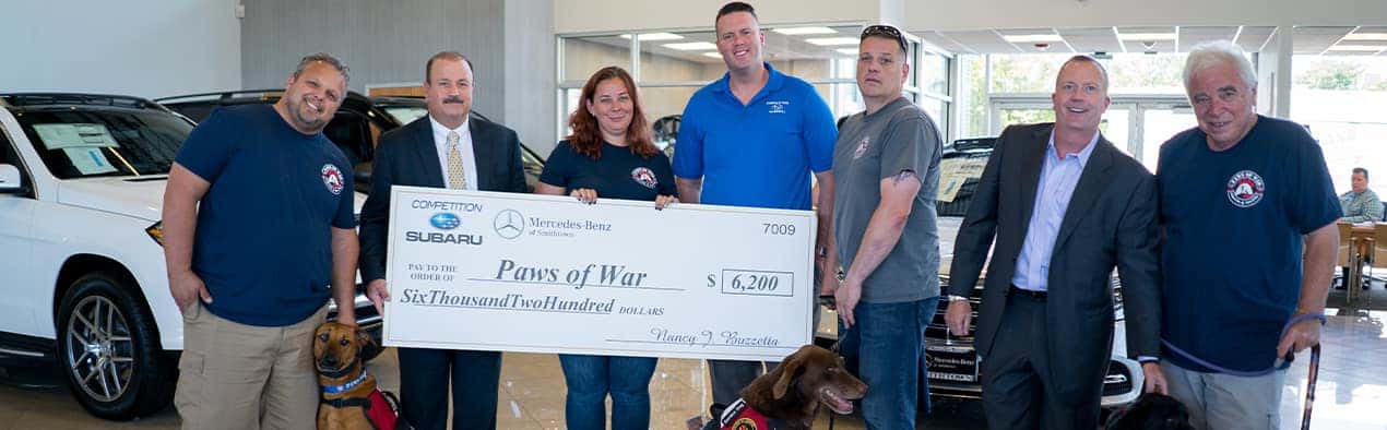 A group of seven people with two service dogs stand with a large check for Paws of War.
