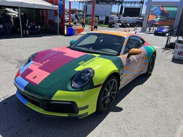 A Porsche sports car with a colorful, geometric paint scheme of green, pink, blue, orange, and yellow.