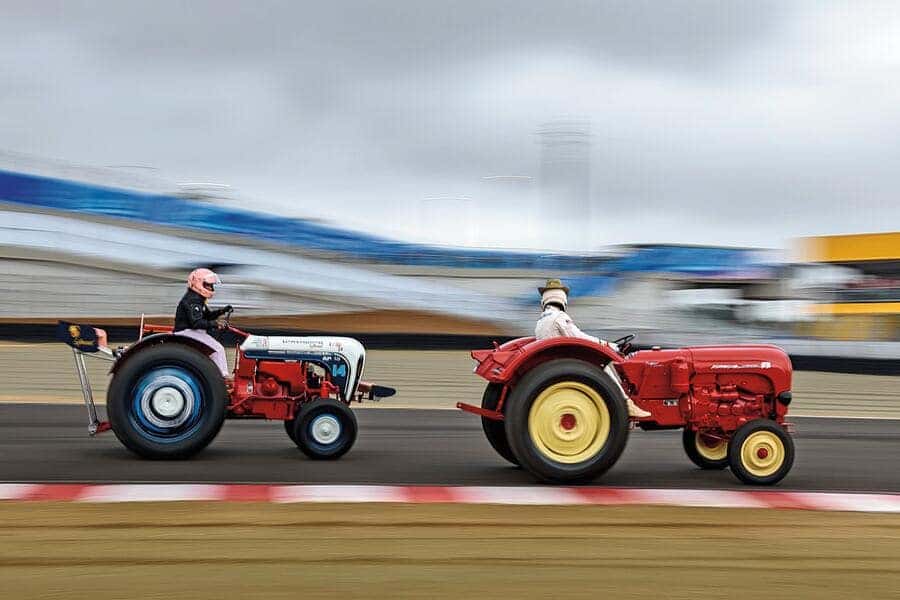 Two brightly painted, vintage tractors, red and red/white/blue, race side-by-side on an asphalt track.