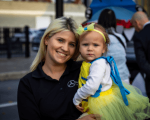 Blonde woman in black shirt holding a baby dressed as a bumblebee.