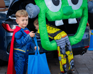 Two children trick-or-treating in costumes from the trunk of a car decorated like a monster face.