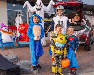 Father in football jersey with three young boys in Sonic, Bumblebee, and Superman costumes, with Halloween decor.